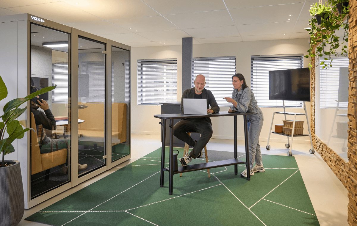 Medewerkers van dpi overleggen aan een hoge tafel naast een afgesloten werkcabine