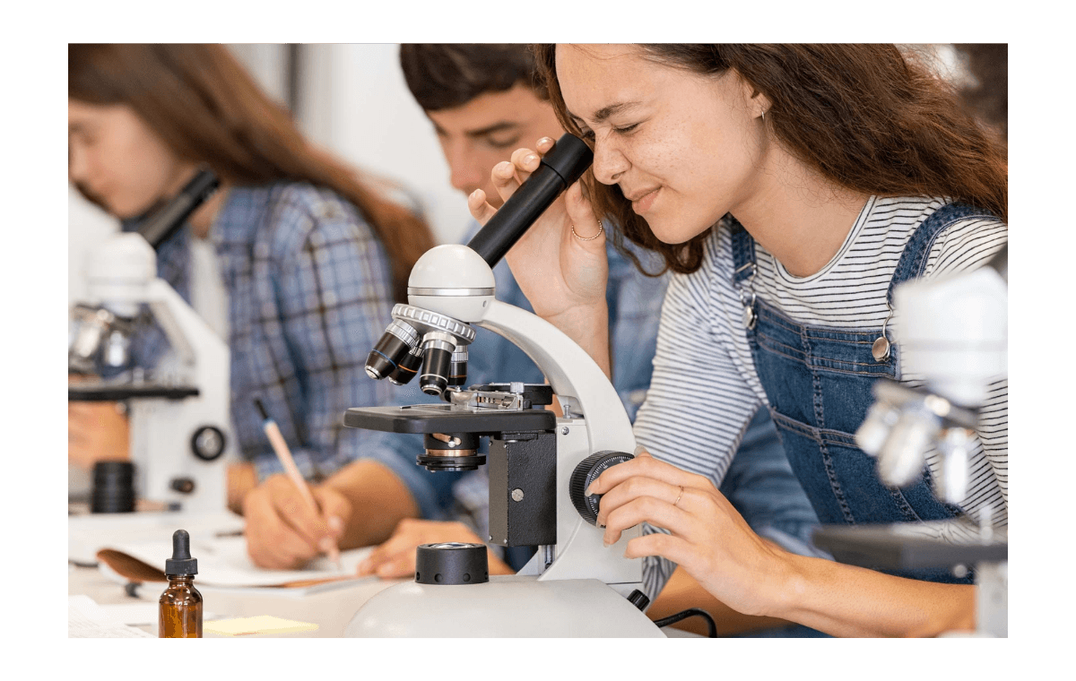 Studente kijkt door een microscoop in een praktijklokaal