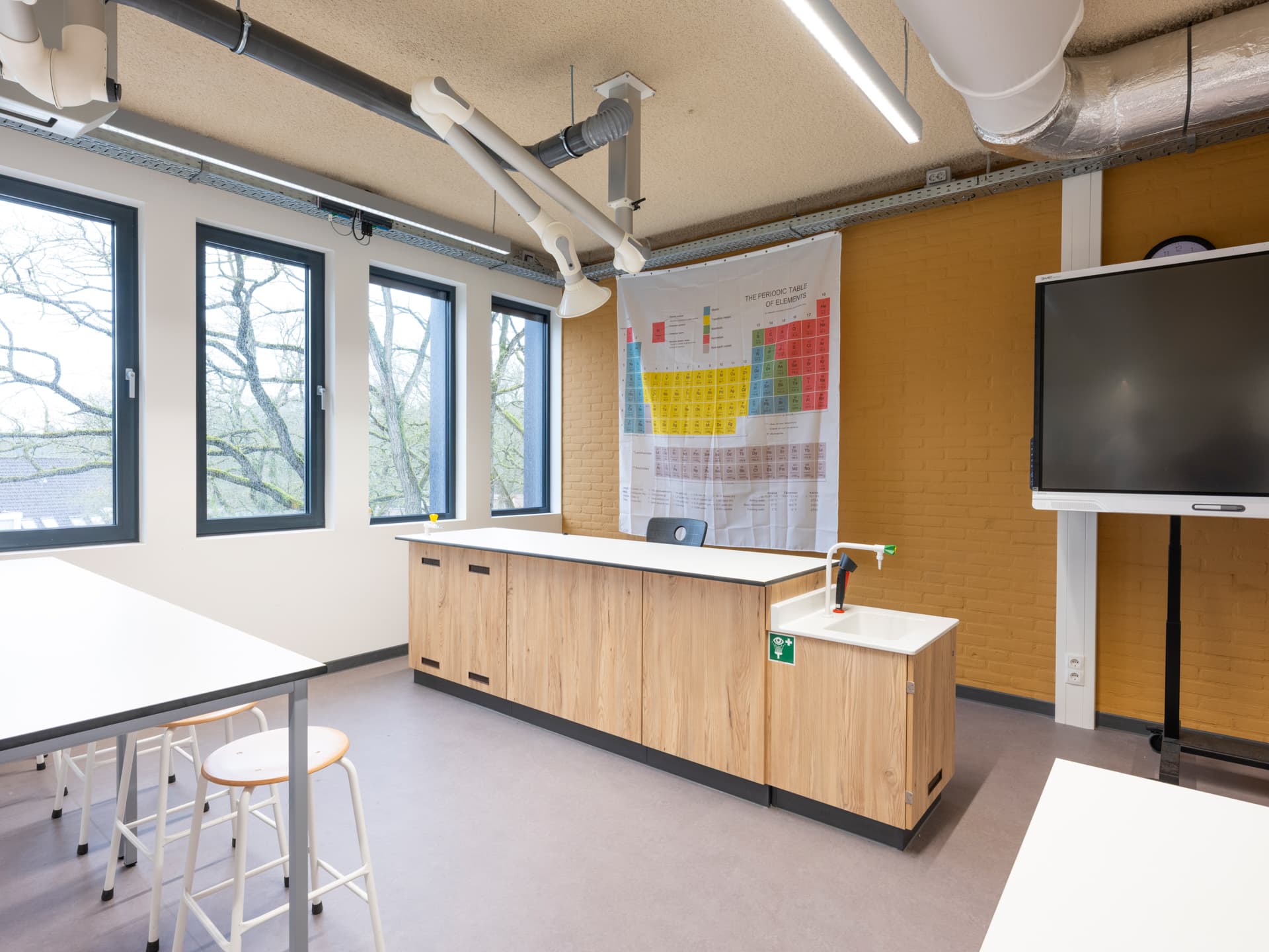 Practicumlokaal met houten demonstratietafel, krukken en digitaal schoolbord
