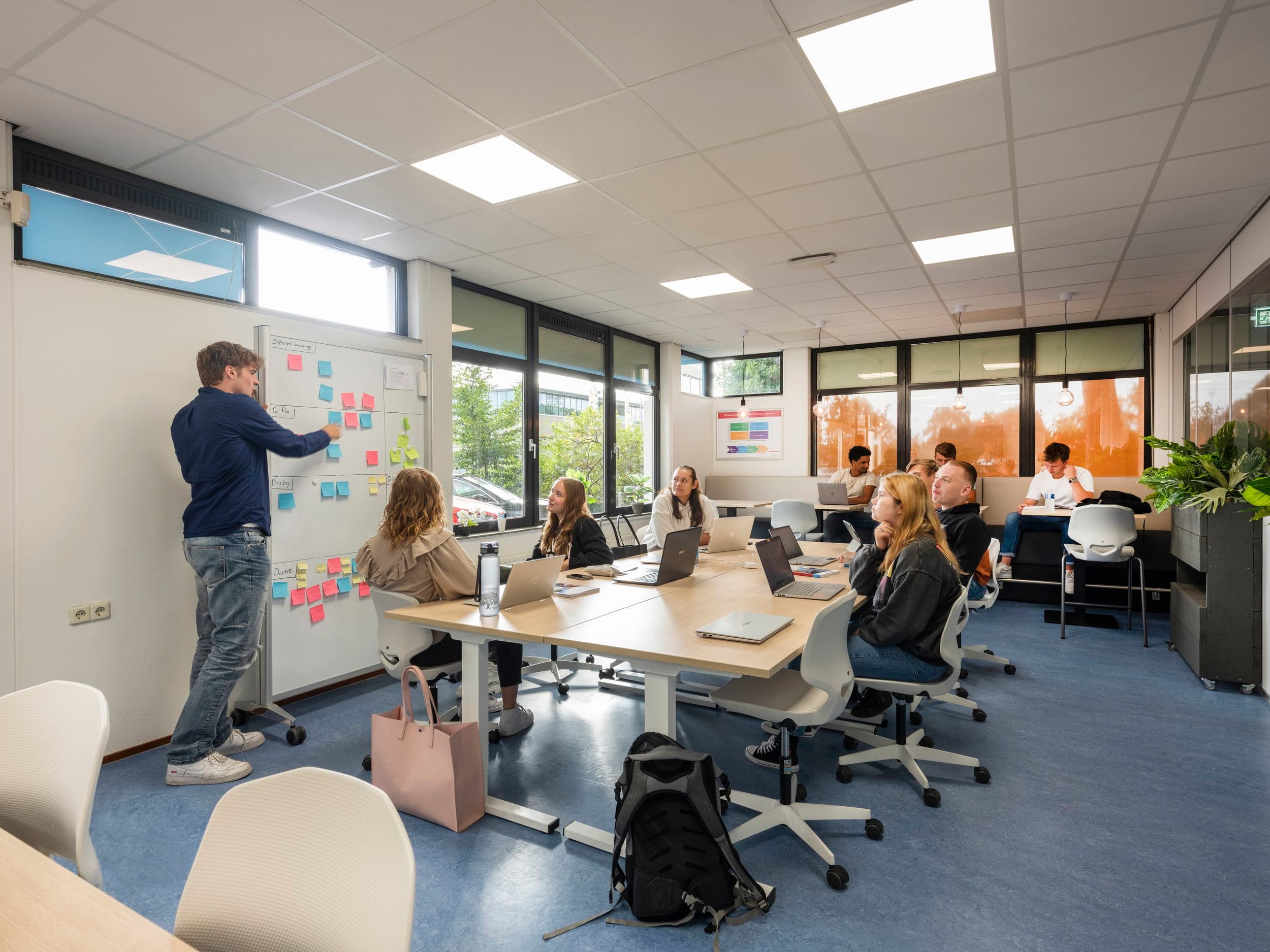 Leerlingen presenteren gezamenlijk een project aan de hand van schetsen en ideeën op een whiteboard in een modern klaslokaal