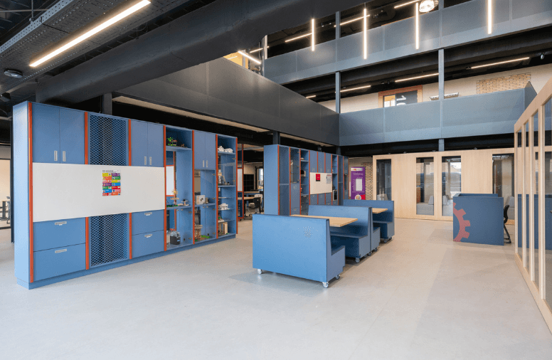 Technieklokaal met blauwe kastenwand, werkbanken en een open vide