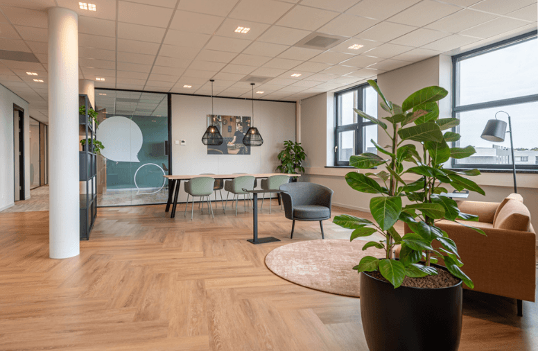 Informele overlegplek met twee fauteuils, een ronde tafel, planten en een glazen scheidingswand
