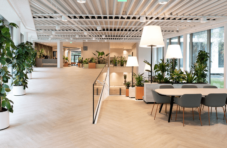 Moderne kantooromgeving met hellingbaan, ronde overlegtafel, planten en houten plafondlamellen