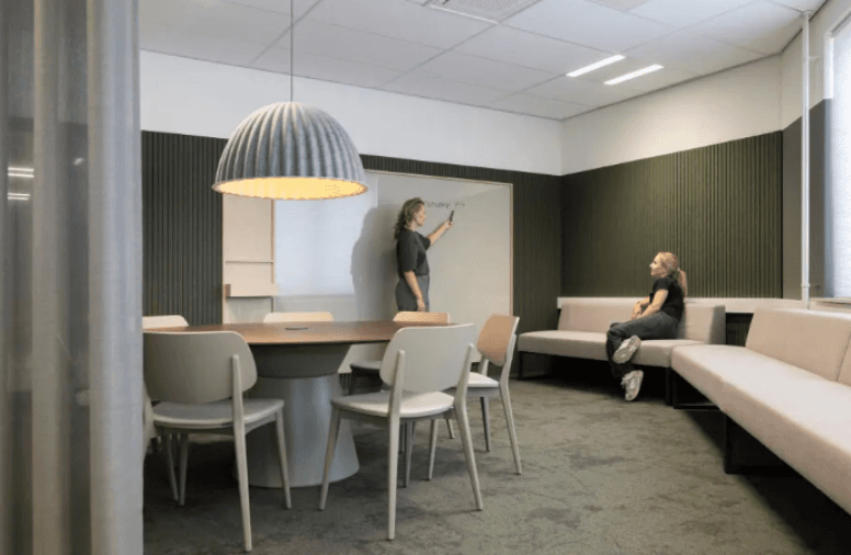 Medewerkers overleggen in een vergaderruimte met lange tafel, zitbank en groene wand
