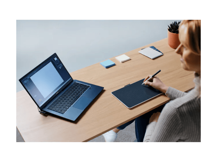 Gebruiker werkt met een tekentablet en laptop aan een bureau.