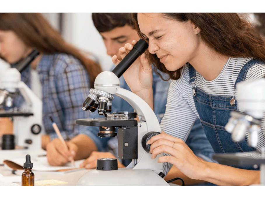Studente kijkt door een microscoop in een praktijklokaal