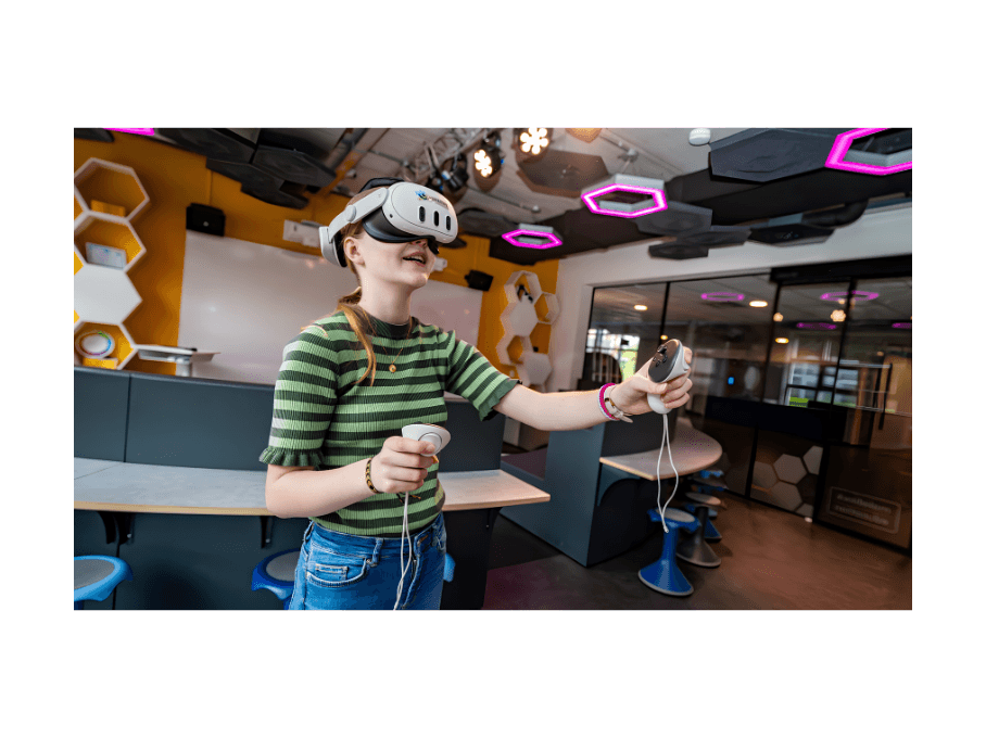 Leerling gebruikt een VR-bril en controllers in een technologielokaal.