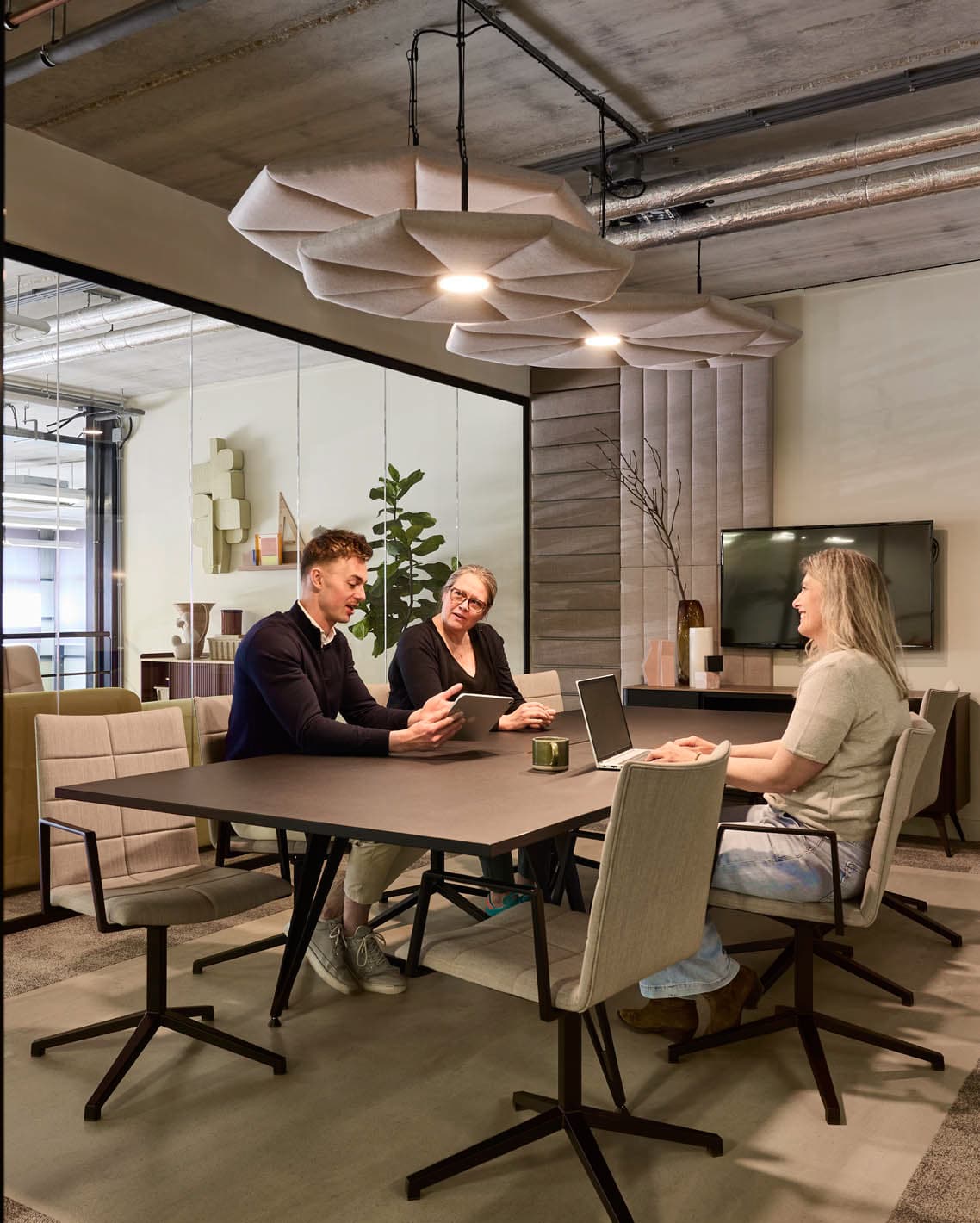 Drie medewerkers overleggen aan een houten tafel in een modern kantoor