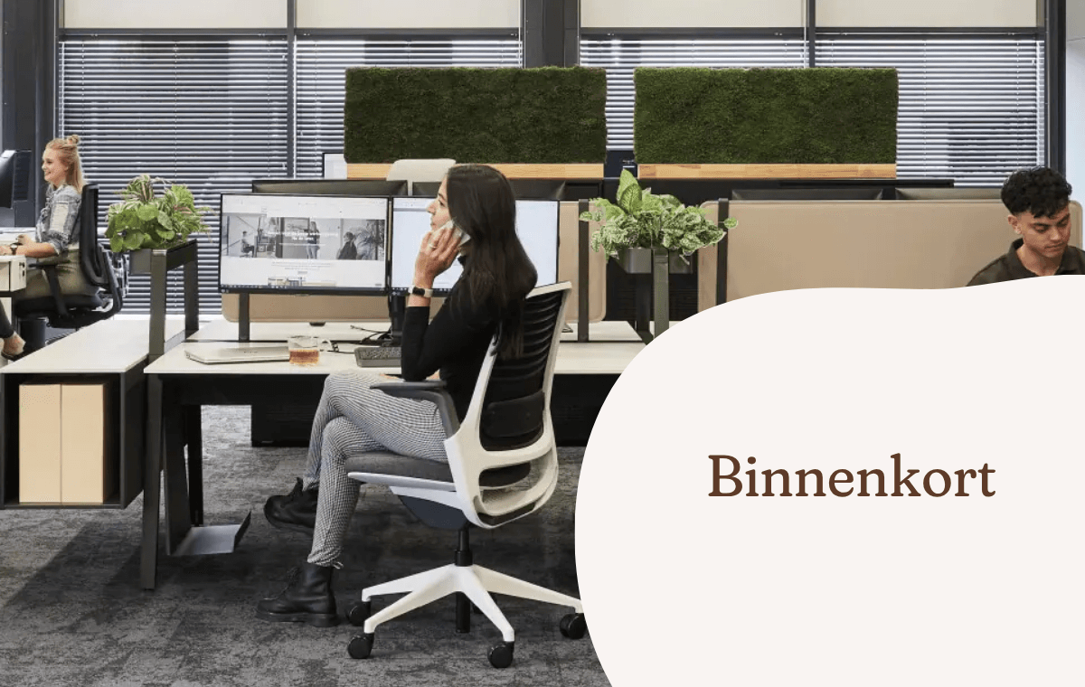 Medewerkers werken aan bureaus in een kantoor met groene scheidingswanden.