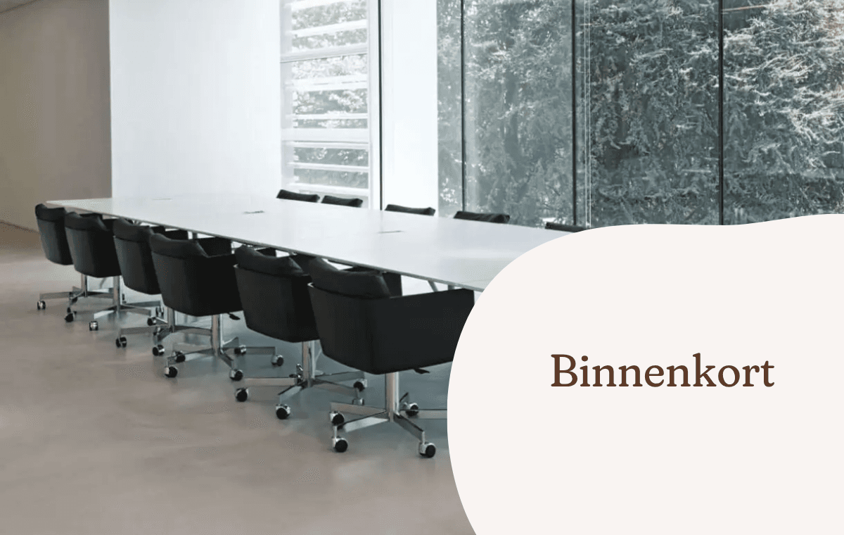Lange vergadertafel met zwarte verrijdbare stoelen in een lichte vergaderruimte.