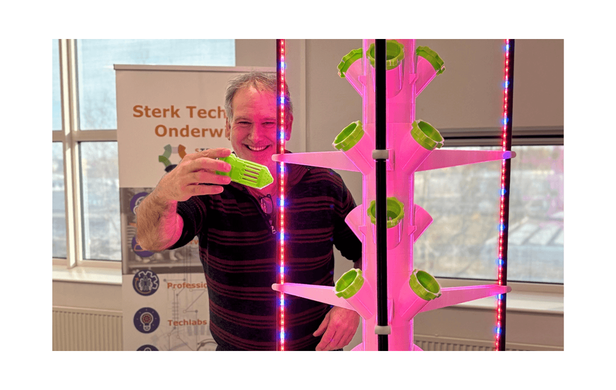 Docent toont een kweekbeker bij een verticale plantenwand met roze groeilampen.
