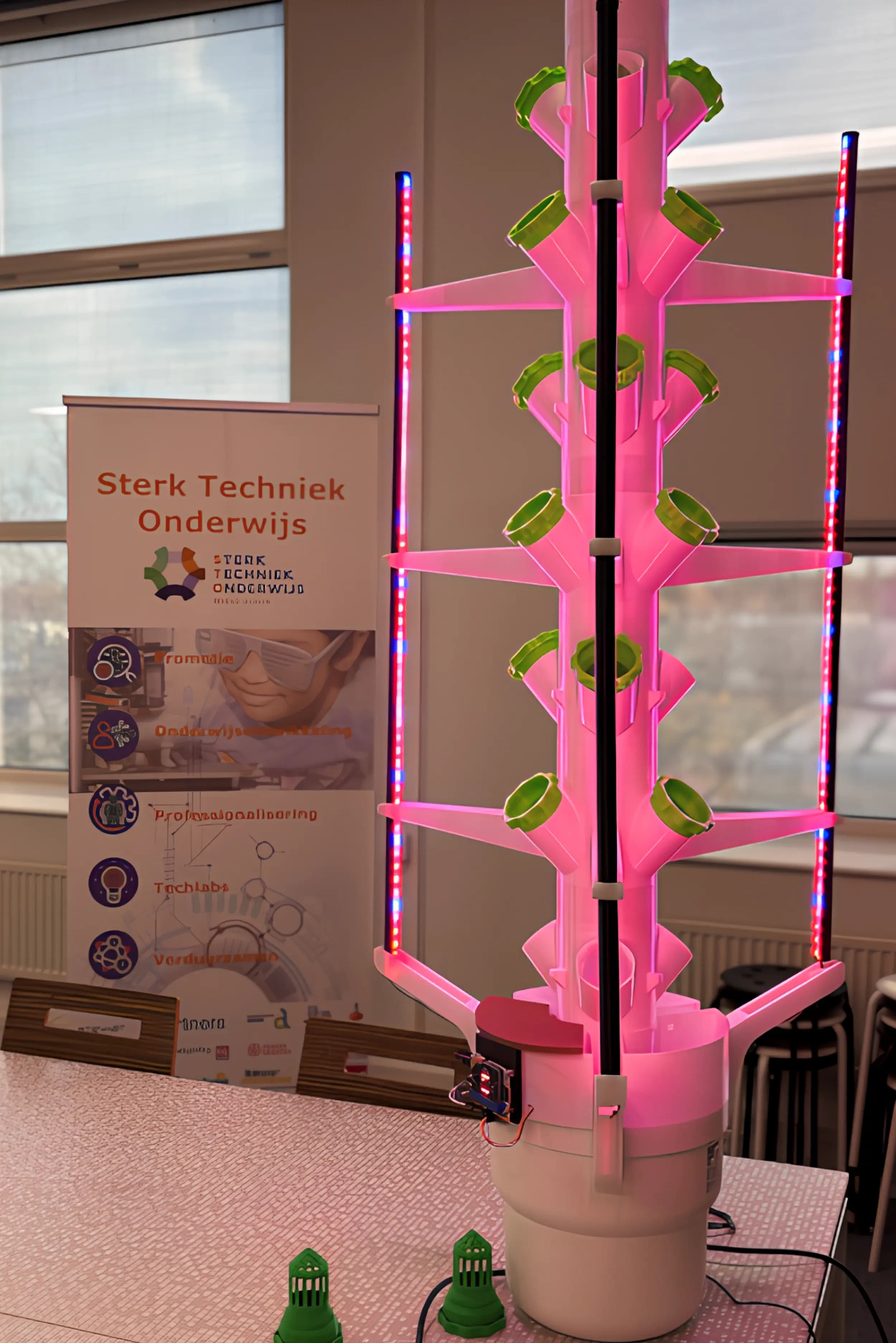 Hydroponic tower met roze groeiverlichting in een technieklokaal.