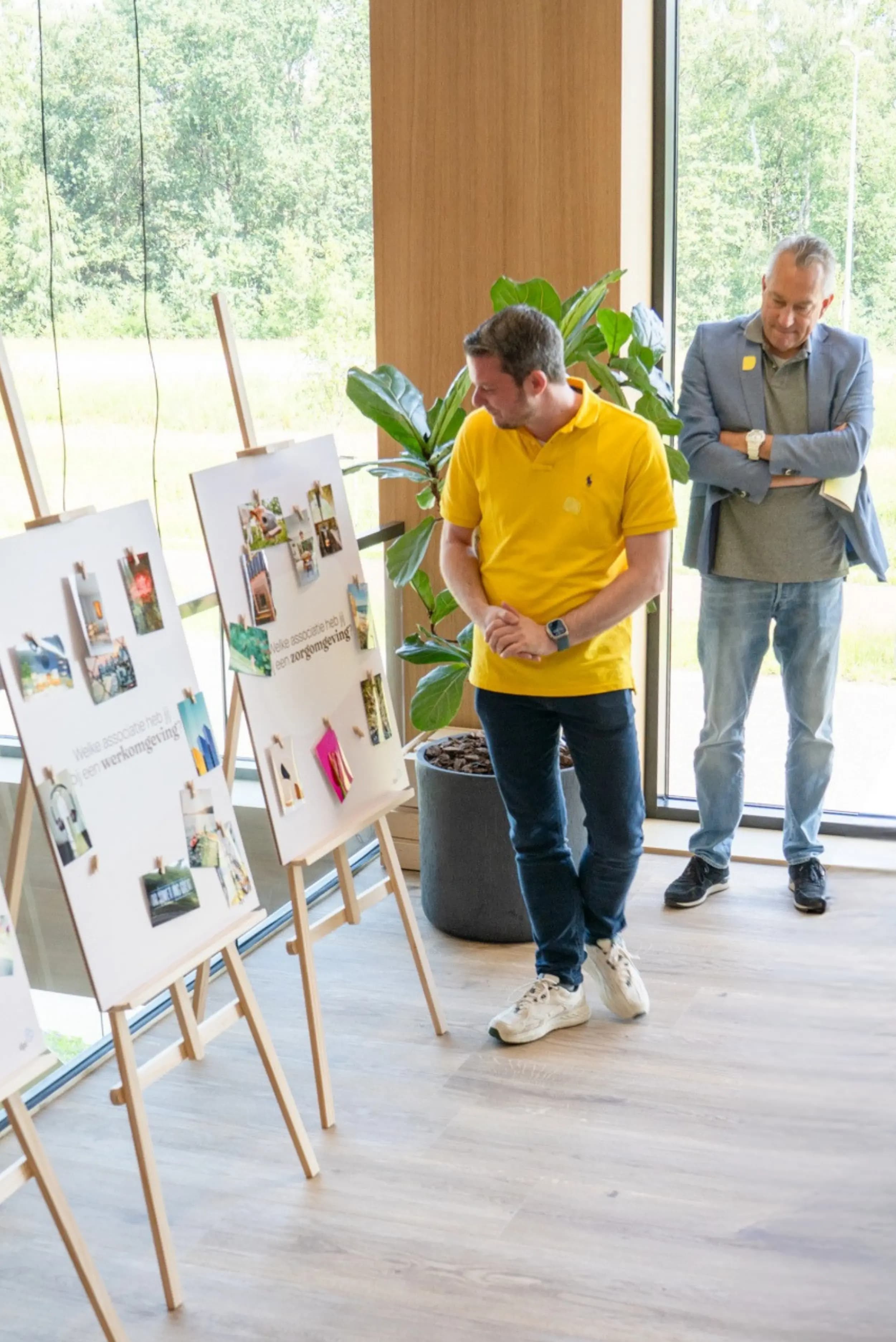Twee medewerkers bekijken moodboards met interieurbeelden op houten schildersezels.