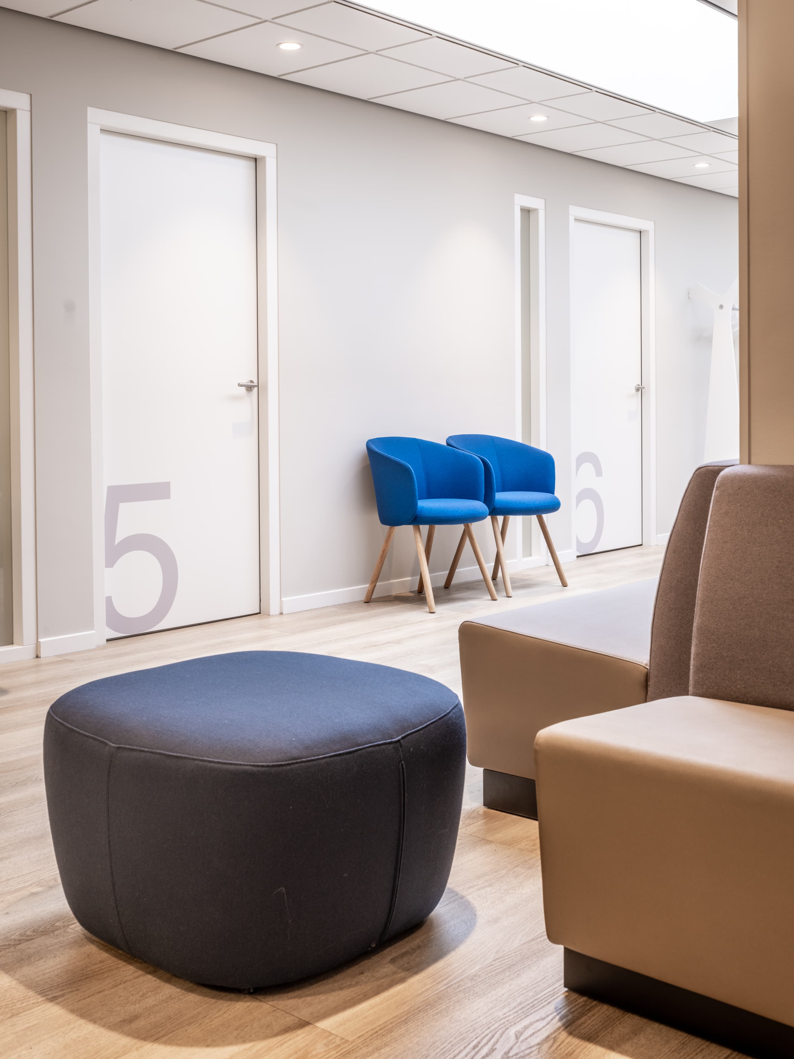 Wachtruimte met een taupekleurige zitbank, blauwe stoelen en een ronde poef