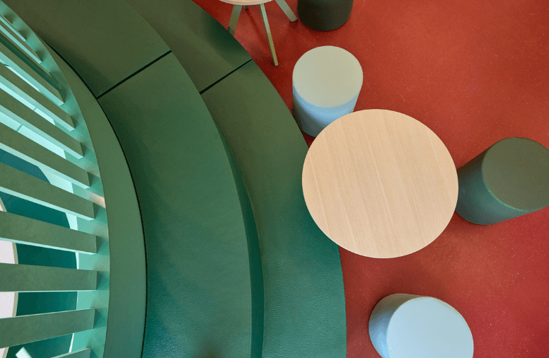 Informele leeromgeving met gebogen groene zitbank, ronde tafel en losse krukken