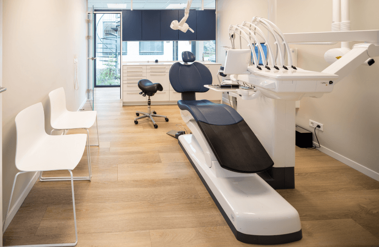 Behandelkamer van een tandartspraktijk met behandelstoel, apparatuur en bezoekersstoelen