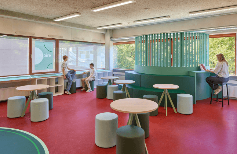 Leerlingen werken in een informele leeromgeving met ronde tafels en een groene zitbank