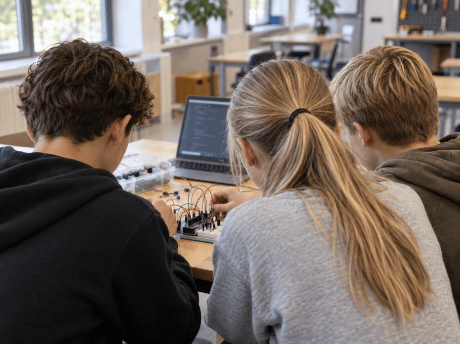 Drie leerlingen werken samen aan een elektronica-opdracht met een microcontroller en bedrading.