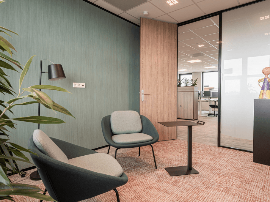 Informele overlegplek met twee fauteuils, een ronde tafel en een groene wand