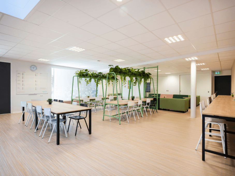 Multifunctionele ruimte met lange tafels, veel zitplaatsen, planten en een loungehoek