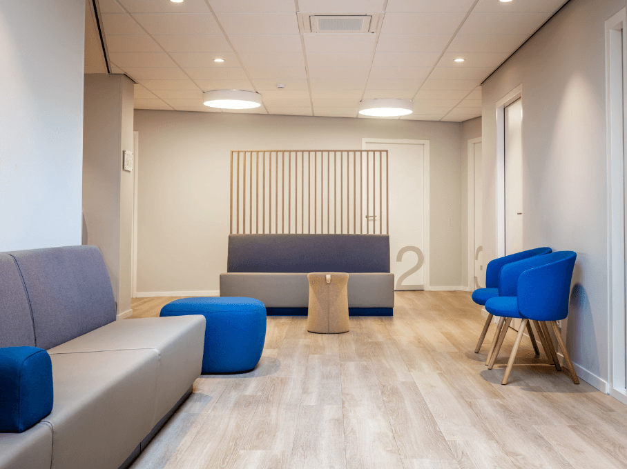 Wachtruimte met grijze banken, blauwe fauteuils en een lage houten tafel