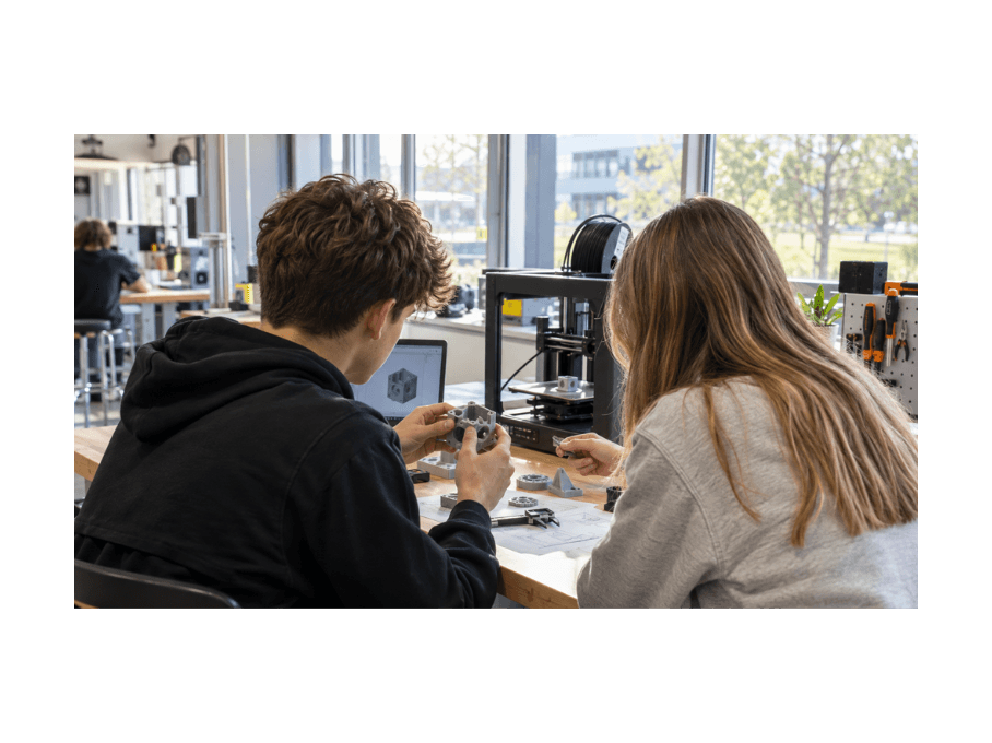 Twee leerlingen werken aan een 3D-geprint prototype naast een 3D-printer in een technieklokaal.